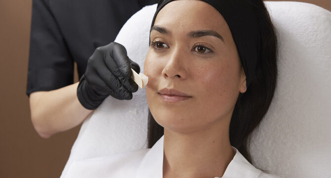 Assistante Dr Olivier CLAUDE appliquant crème à la spatule dans le cadre d'un traitement sur beau visage de femme naturelle