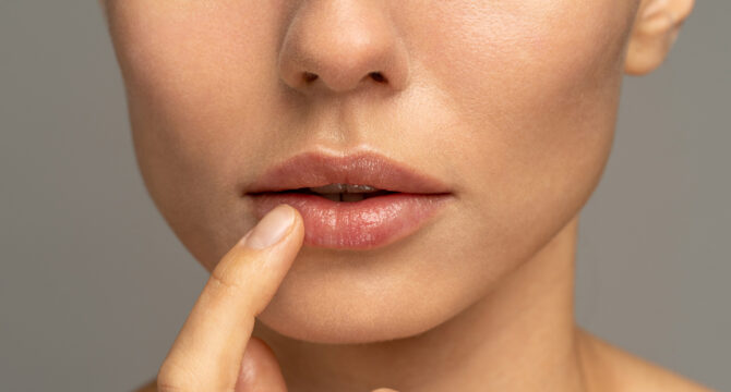 Close up of woman applying moisturizing nourishing balm to her lips with her finger to prevent dryness and chapping in the cold season