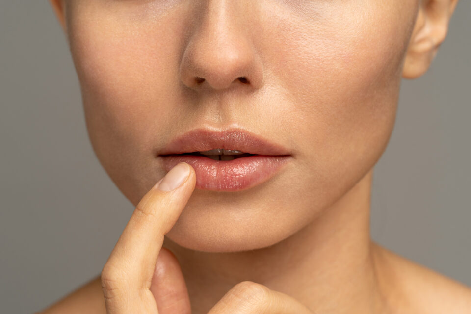 Close up of woman applying moisturizing nourishing balm to her lips with her finger to prevent dryness and chapping in the cold season